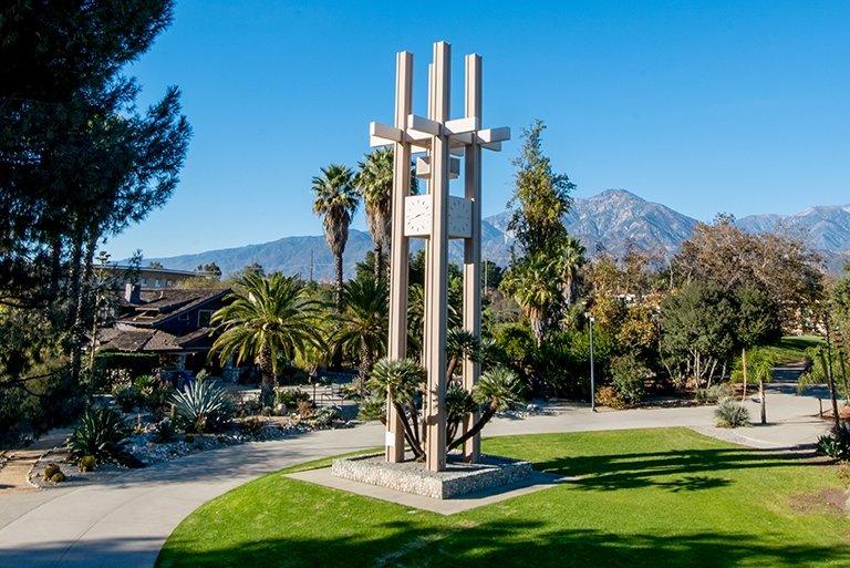 A view of the Pitzer Clock Tower on a bright day with the grove house and the san bernardino mountains behind it. 